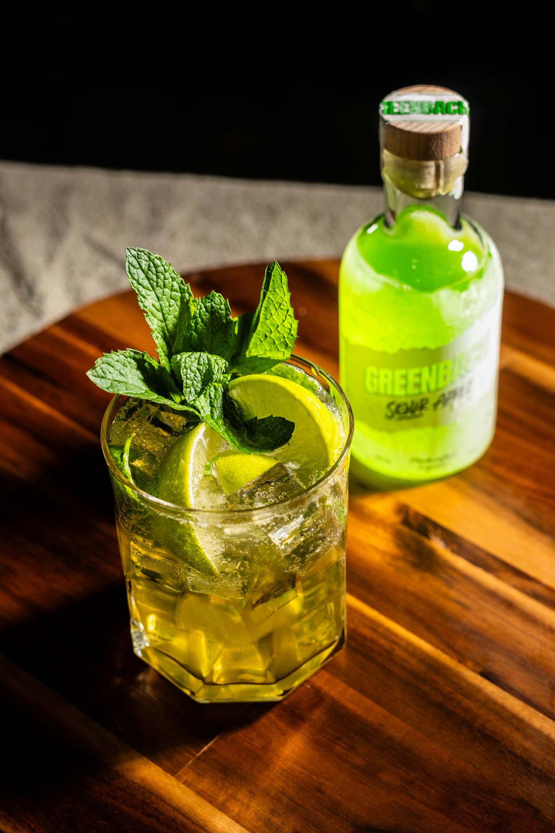 A tall Greenbach serve with mint and citrus beside the bottle