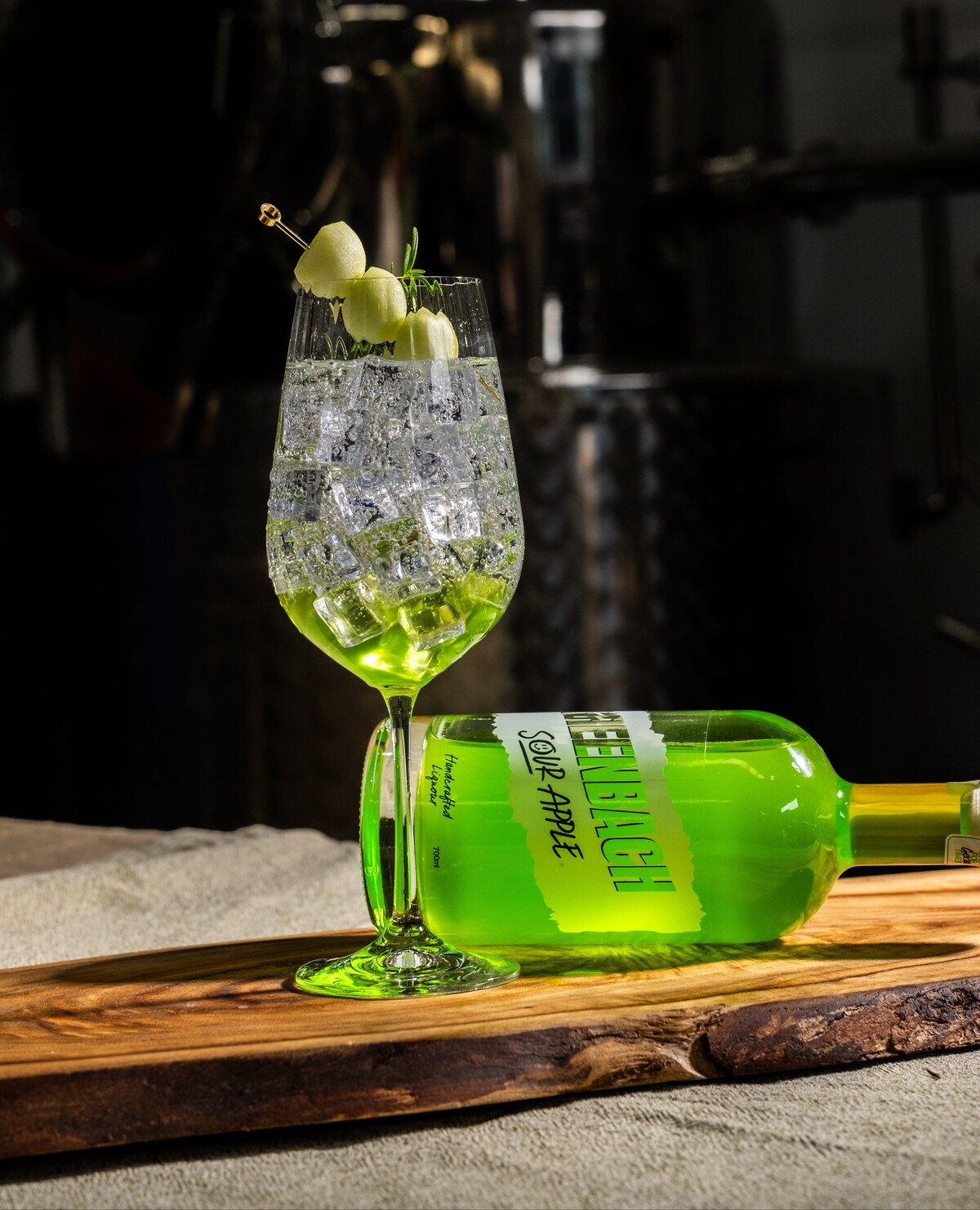 A Greenbach spritz in a wine glass, packed with ice, melon on a pick